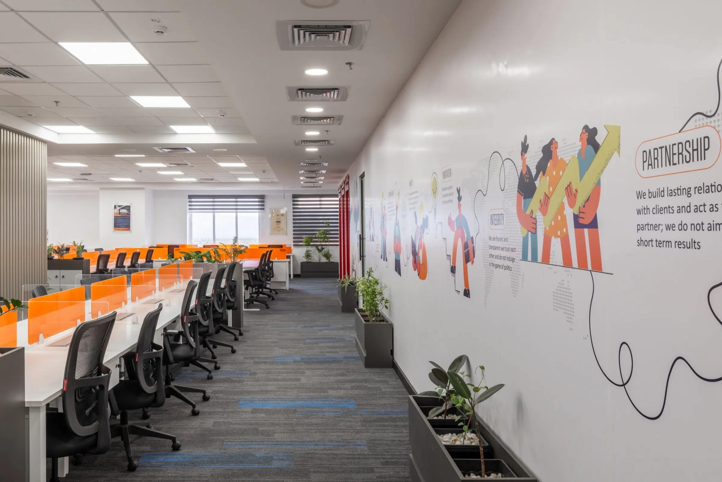 Open-plan workstations with orange screens beside a hand-drawn "Partnership" mural wall